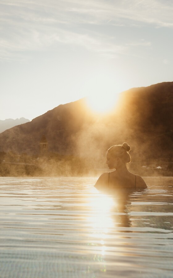 Frau im Pool bei Sonnenaufgang mit Bergblick
