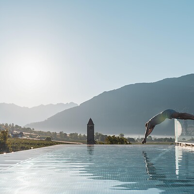 Uomo che si tuffa nella Sky Infinity Pool con vista sulle montagne e il sole basso all’orizzonte