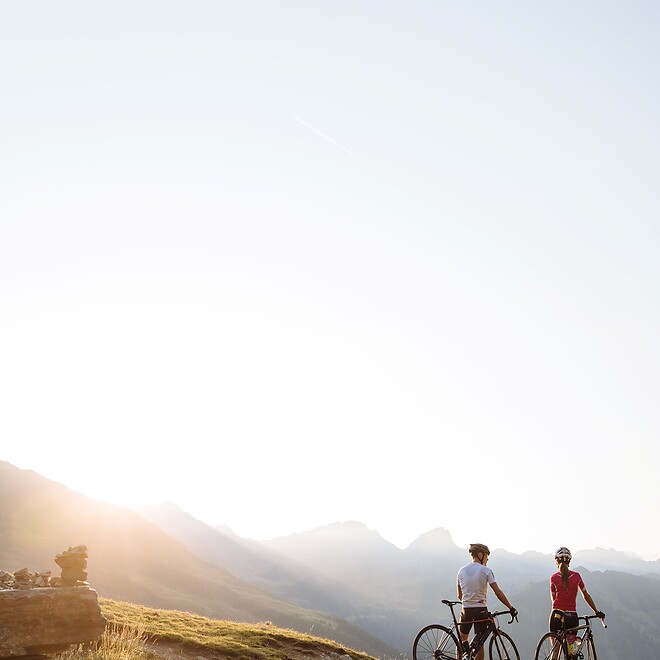 Donna e uomo con le bici davanti a un panorama montano al tramonto