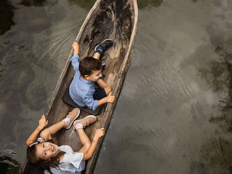Famiglia che naviga con una barca di legno lungo un piccolo canale alpino