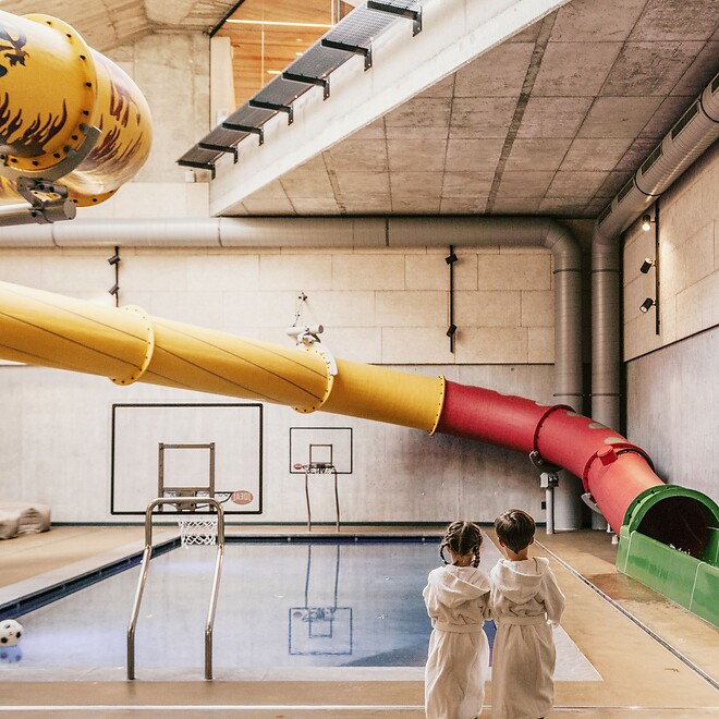 Ragazza e ragazzo davanti a una grande piscina interna con scivolo ad acqua a tubo