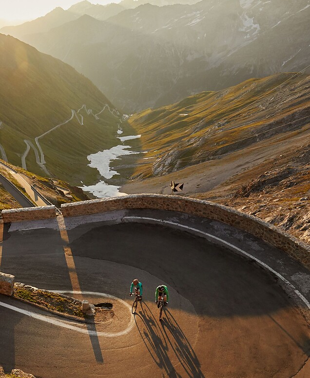Ciclisti che percorrono le curve dello Stelvio al tramonto con il sole basso