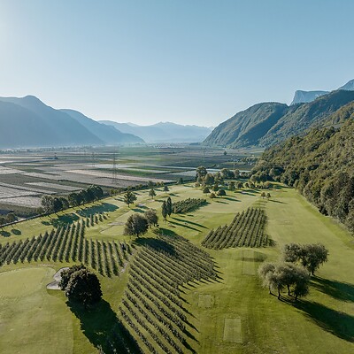 Ripresa con drone di un campo da golf tra frutteti di mele e montagne