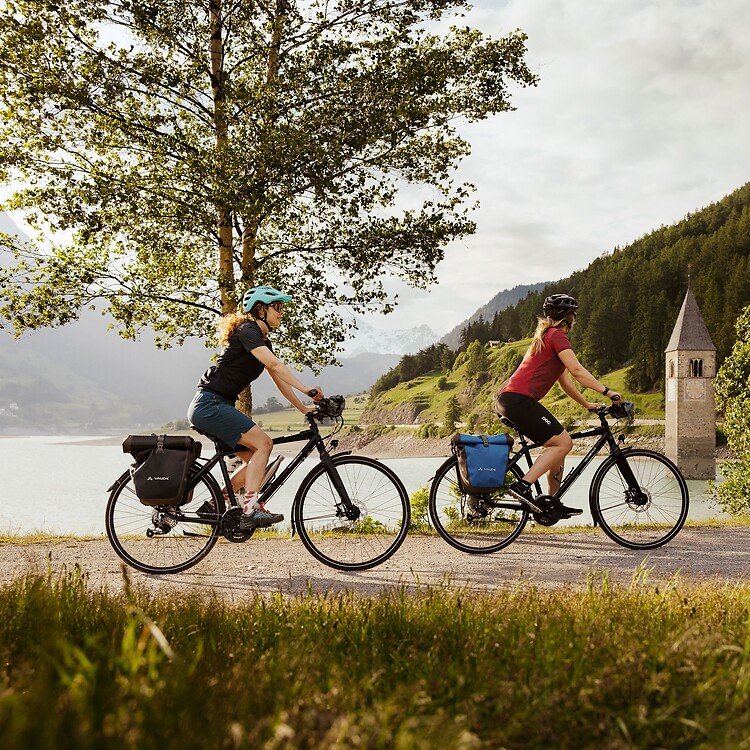 Due donne in e-bike passando davanti alla torre sommersa nel Lago di Resia