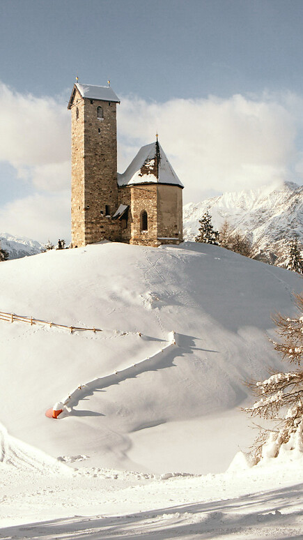 Chiesetta su collina in inverno con neve e panorama montano