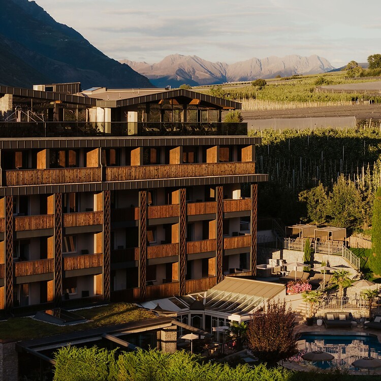 Hotelfassade mit Pool und Garten umgeben von der Bergwelt im Vinschgau