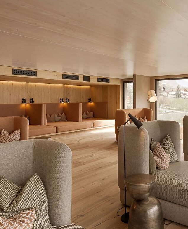 Moderna sala relax in legno con lettini imbottiti e vetrata con panorama montano