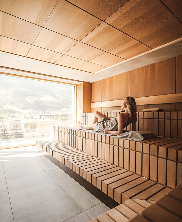 Donna sdraiata in sauna con panorama montano e luce solare delicata