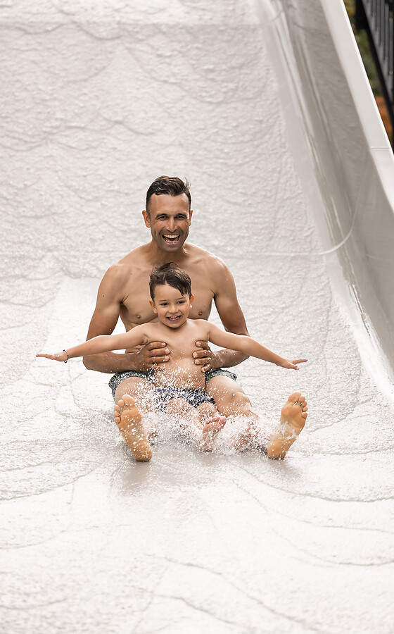 Father and son slide down the wave water slide in the hotel garden.
