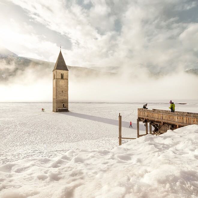 Submerged tower in Lake Resia with snow-covered winter landscape