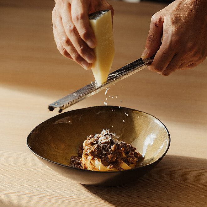 Il cameriere grattugia il formaggio Parmigiano sulla pasta fresca