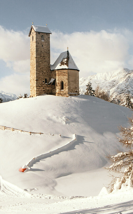 Chiesetta su collina in inverno con neve e panorama montano