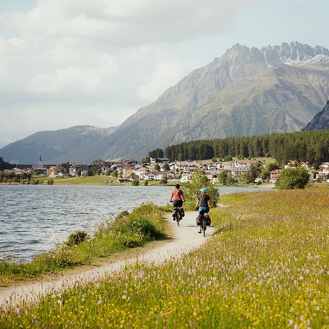 Two women biking on the Reschensee trail past blooming meadows