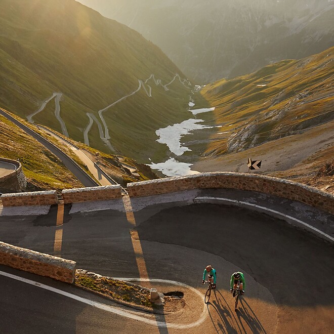 Cyclists riding the switchbacks of Stelvio Pass in the low evening sun
