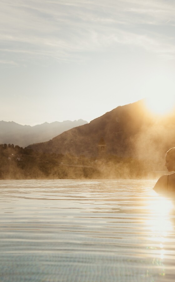 Woman in a pool at sunrise with a mountain view