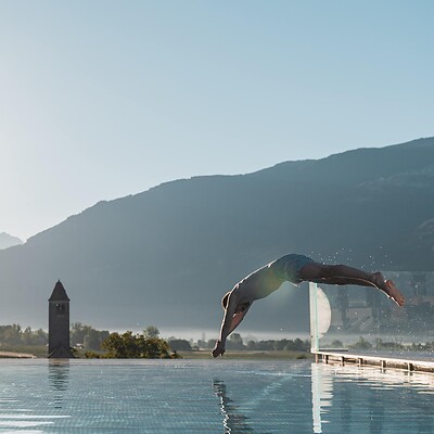 Man diving into the sky infinity pool with mountain views and the low sun