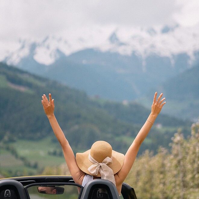 Woman stretching her arms out of Porsche convertible on alpine road
