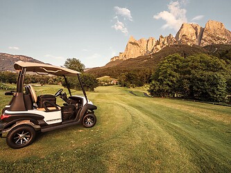 Golf cart on golf course with Dolomites at sunset