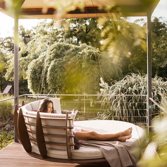 Frau liegt entspannt auf der Hängeliege im großzügigen Hotelgarten
