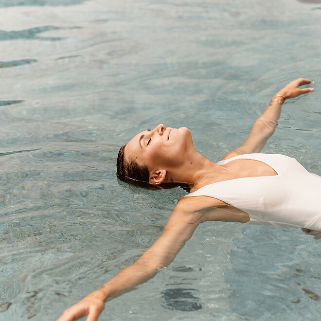 Donna che si lascia galleggiare rilassata nell’acqua della piscina naturale