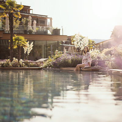 Frau sitzt am Naturpool im mediterranen Hotelgarten im Frühling