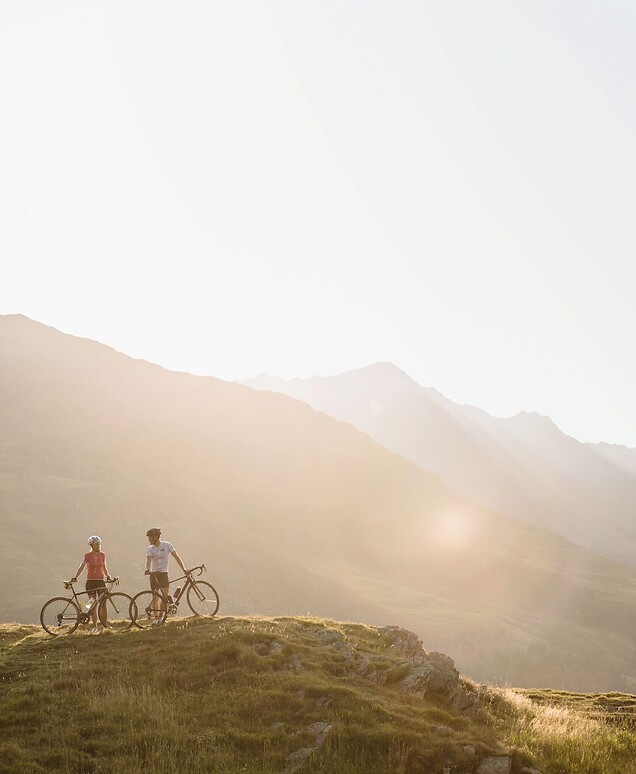 Mann und Frau mit Rennrad bei Sonnenaufgang am Berg