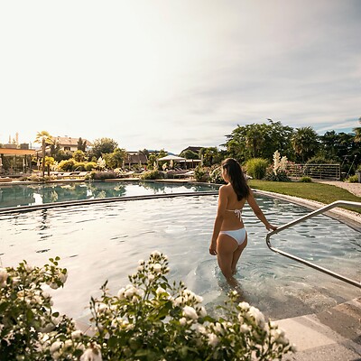 Woman in the natural pool surrounded by the blooming garden landscape