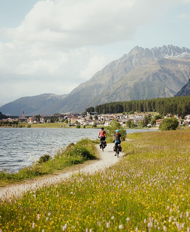 Two women biking on the Reschensee trail past blooming meadows