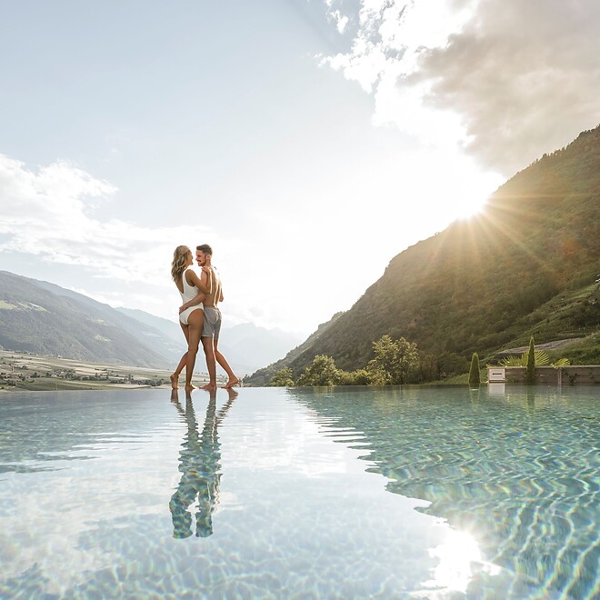 Frau und Mann stehen am Infinity Sky Pool und genießen den Bergblick bei Sonnenuntergang