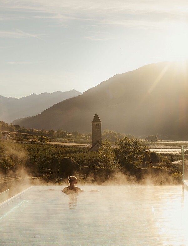 Frau genießt im Infinity Skypool die traumhafte Aussicht bei Sonnenaufgang