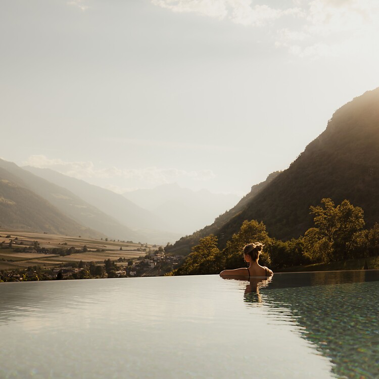 Frau genießt im Infinity Pool bei Sonnenuntergang die Panoramaaussicht