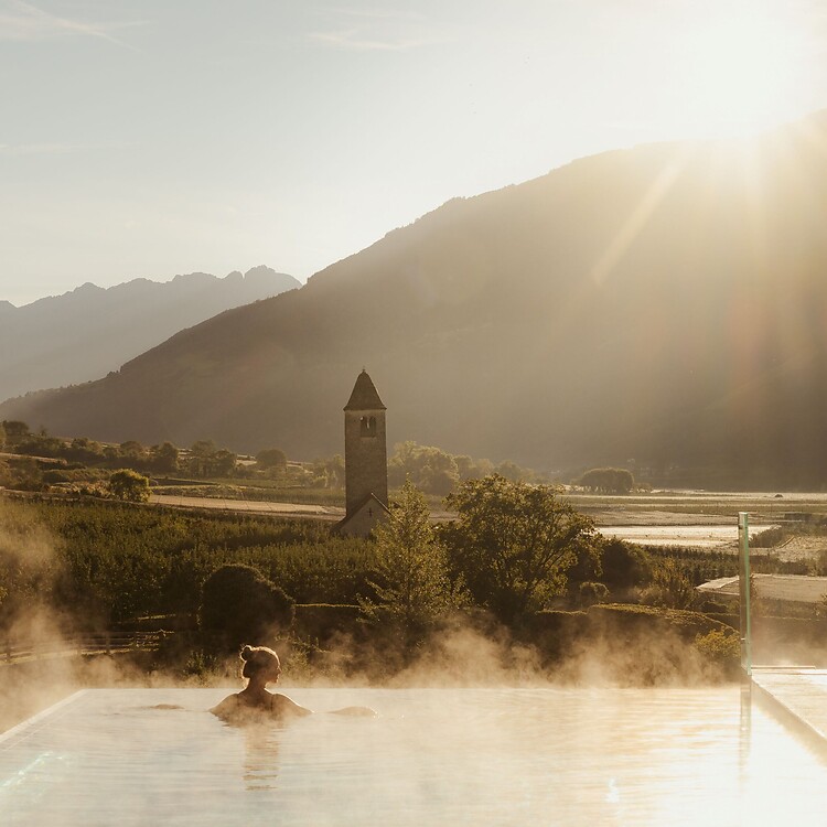 Frau genießt im Infinity Skypool die traumhafte Aussicht bei Sonnenaufgang