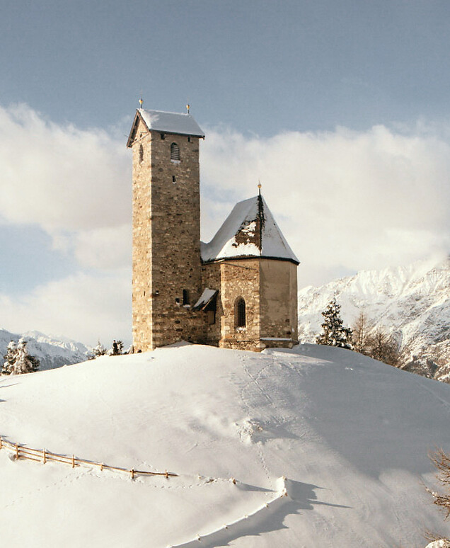 Kirchlein auf Hügel im Winter mit Schnee und Bergpanorama