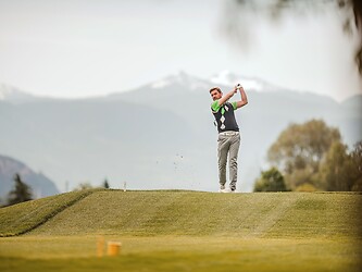 Mann am golfen und umgeben von Bergen