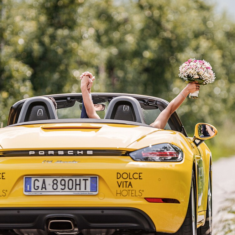 Frau und Mann fahren gelbes Porsche Cabrio in den Flitterwochen