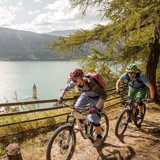 Uomo e donna in bicicletta su un sentiero sopra il Lago di Resia