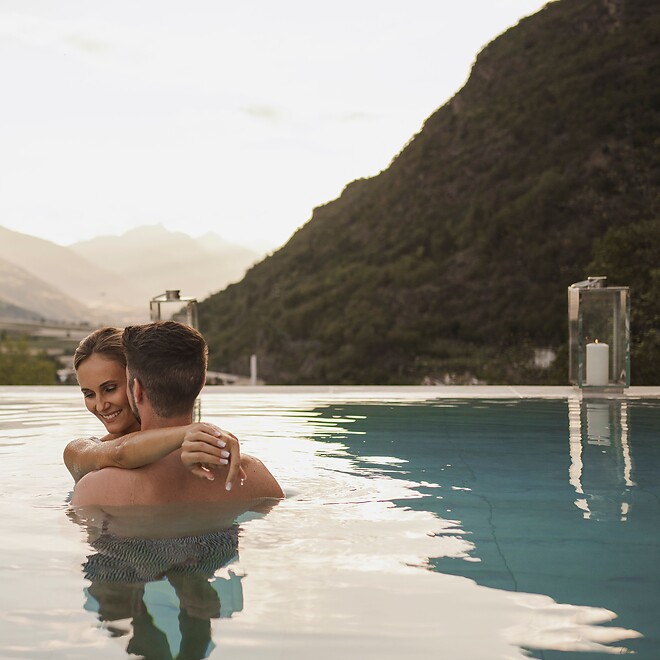 Man and woman hugging in Sky Pool by candlelight with mountain panorama
