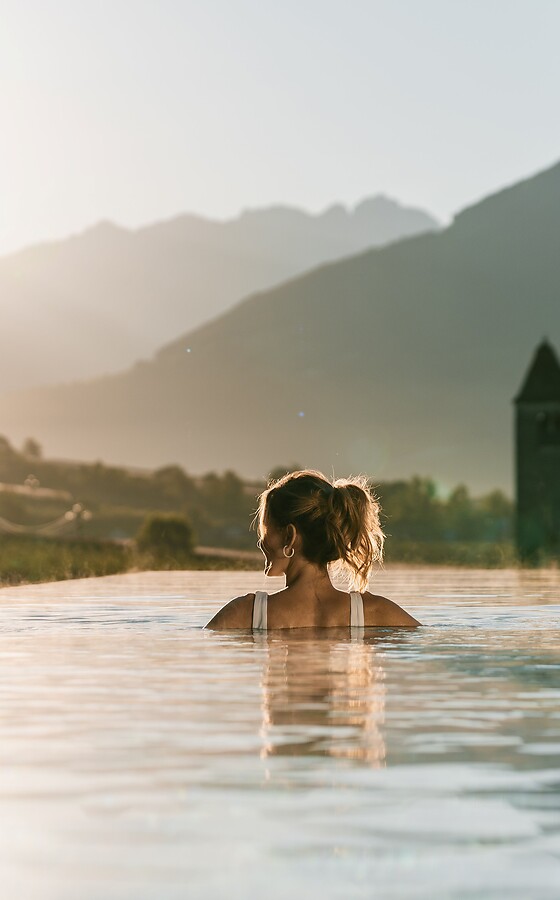 Rückenansicht von Frau in Sky Infinity Pool bei rötlich leuchtender Abendsonne