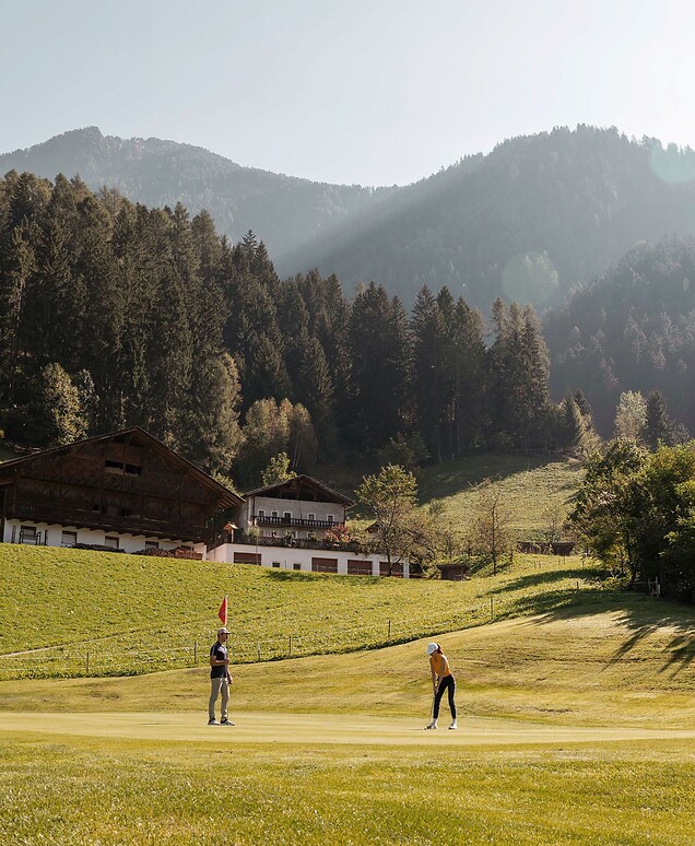 Uomo e donna giocano a golf davanti alle Alpi