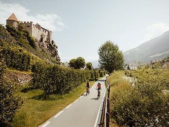 Donna e uomo pedalano su una strada asfaltata passando davanti a un castello