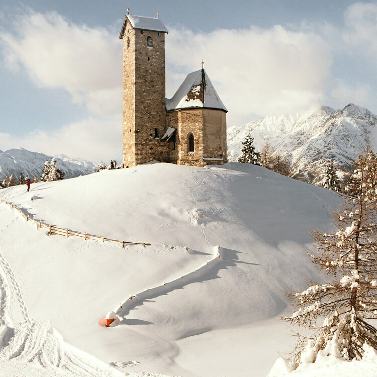 Small church on hill in winter with snow and mountain panorama