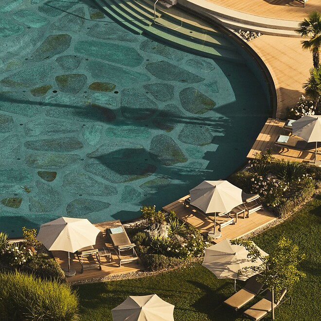 Piscina naturale con lettini prendisole nel giardino mediterraneo dell'hotel