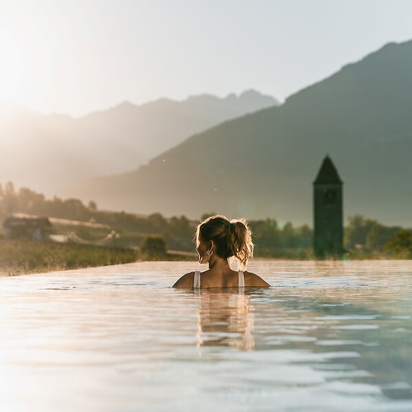 Rückenansicht von Frau in Sky Infinity Pool bei rötlich leuchtender Abendsonne